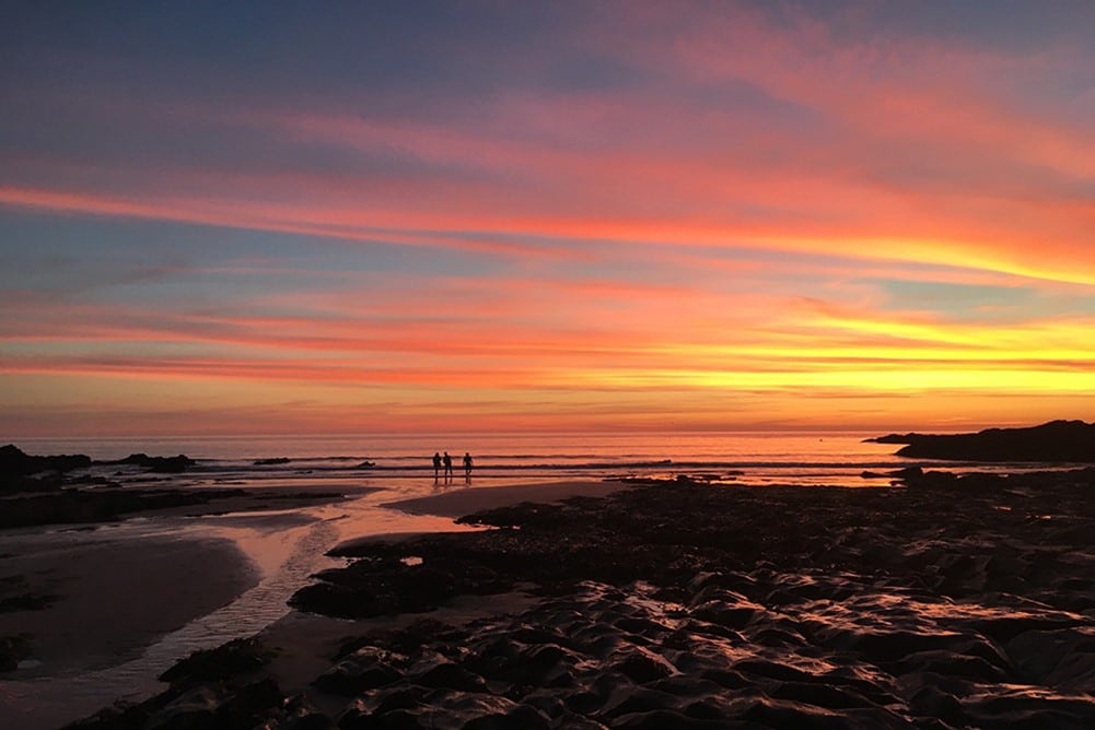 A group of people on a beach at sunset.