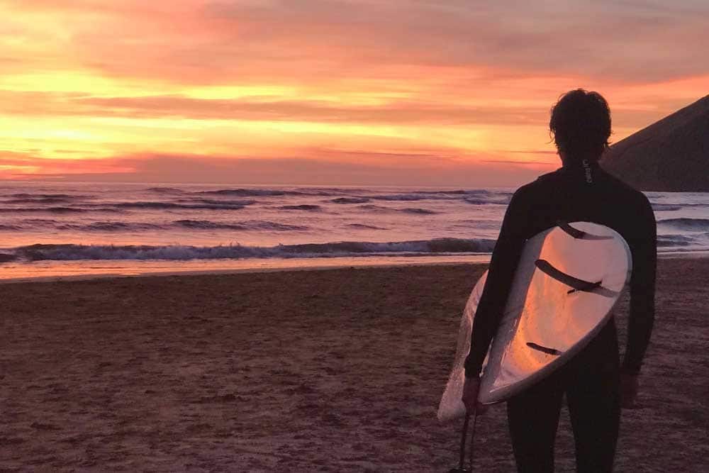 Surfer looking out across a sunset beach.