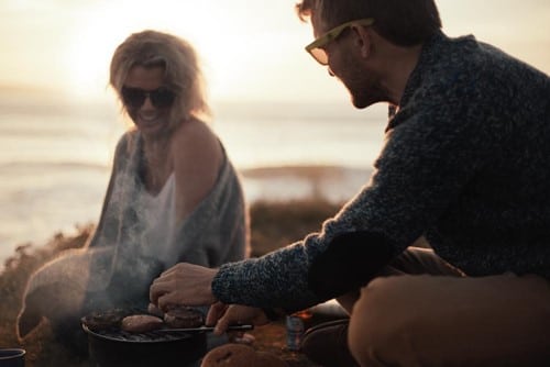A man and woman cooking food on a grill. 