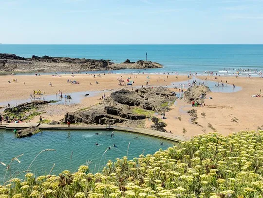 A beach with a natural pool, rocks and people sunbathing.