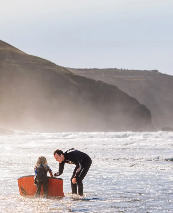 A man teaching a child with a small orange surfboard.