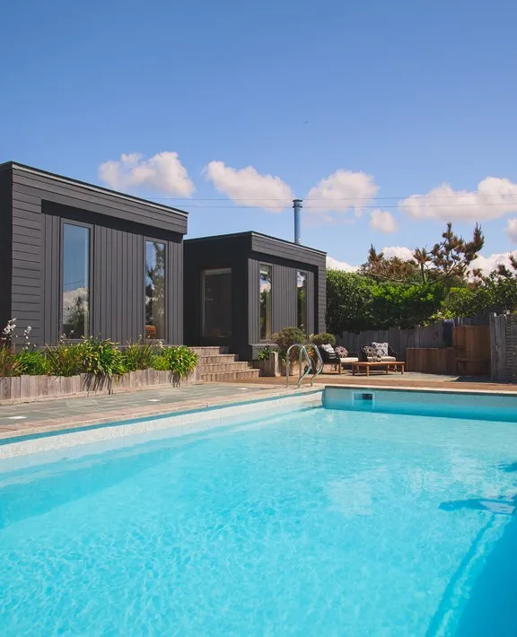 Modern pool overlooked by dark wooden properties.