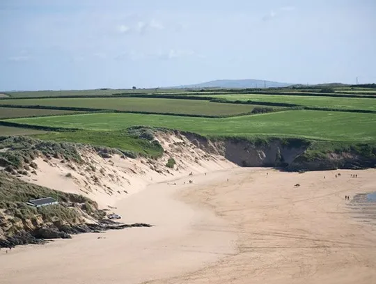 Green fields fading into a sand dune beach.