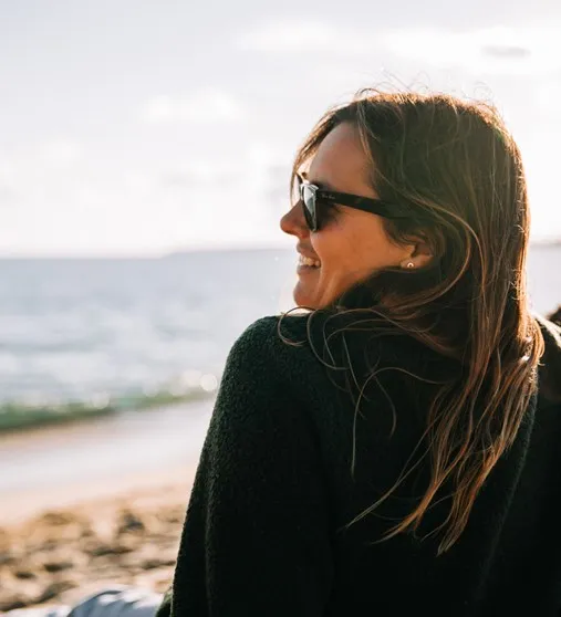 Woman with sunglasses laughing on the beach.