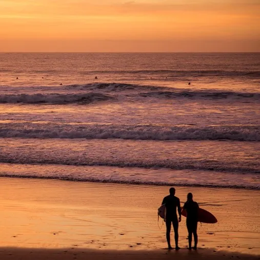 Surfers looking out to sea at sunset.