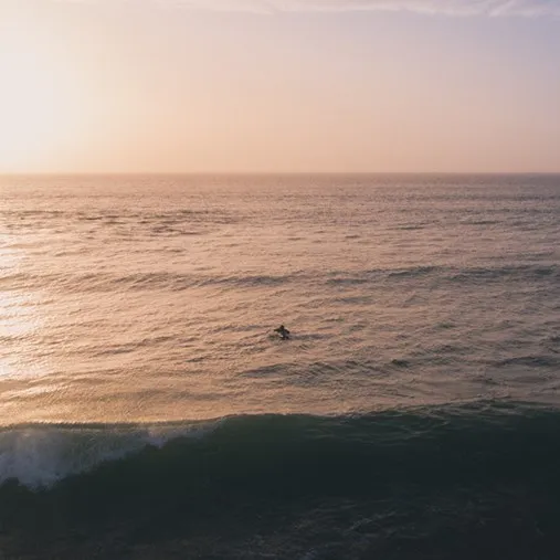 A person swimming in the ocean at sunset.