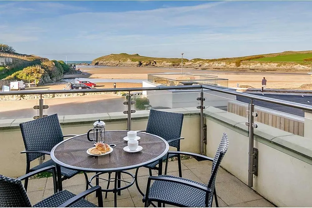 A table and chairs on a balcony overlooking a beach. 