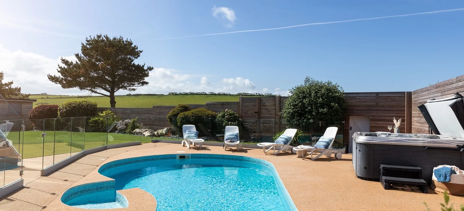 A pool with chairs, a hot tub and a fence.