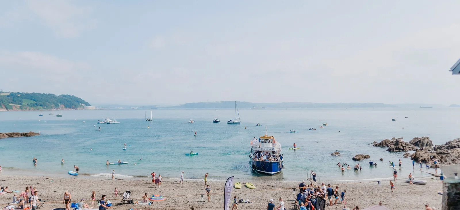 People on a beach with a blue boat in the water.