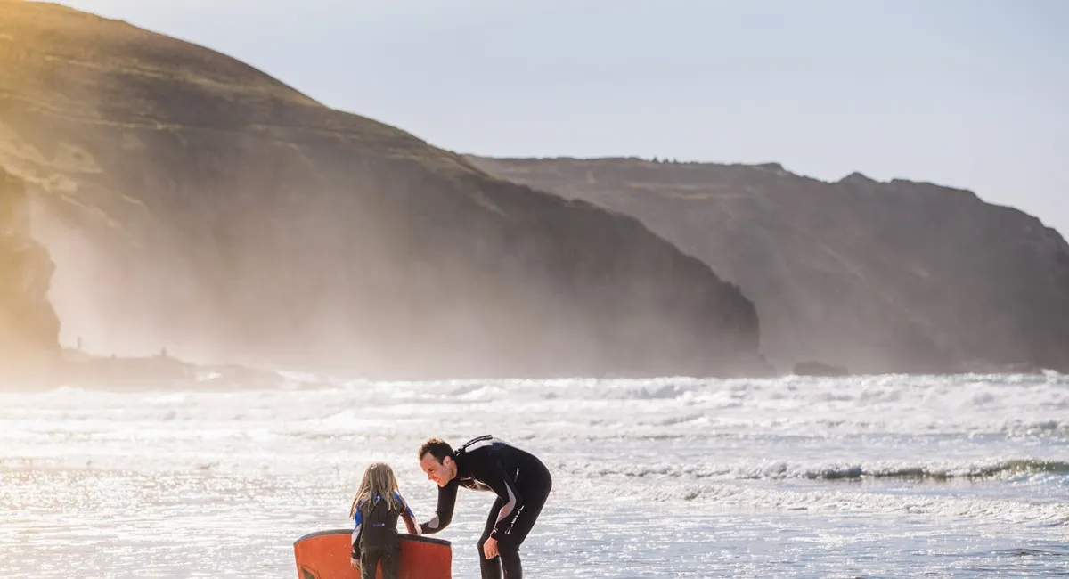 A man and child on a beach with a red boogie board.