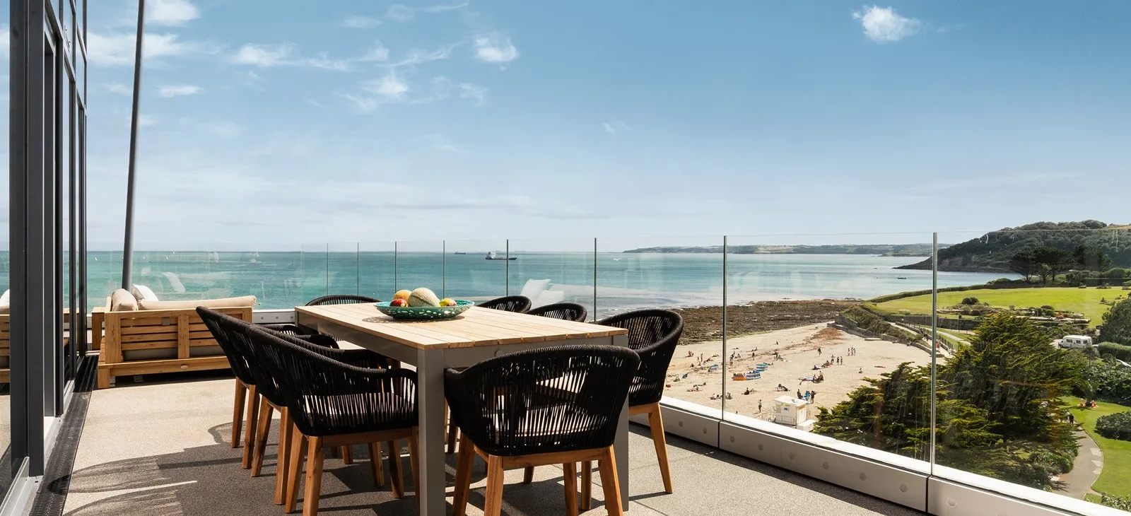 A table and chairs on a balcony overlooking a beach.