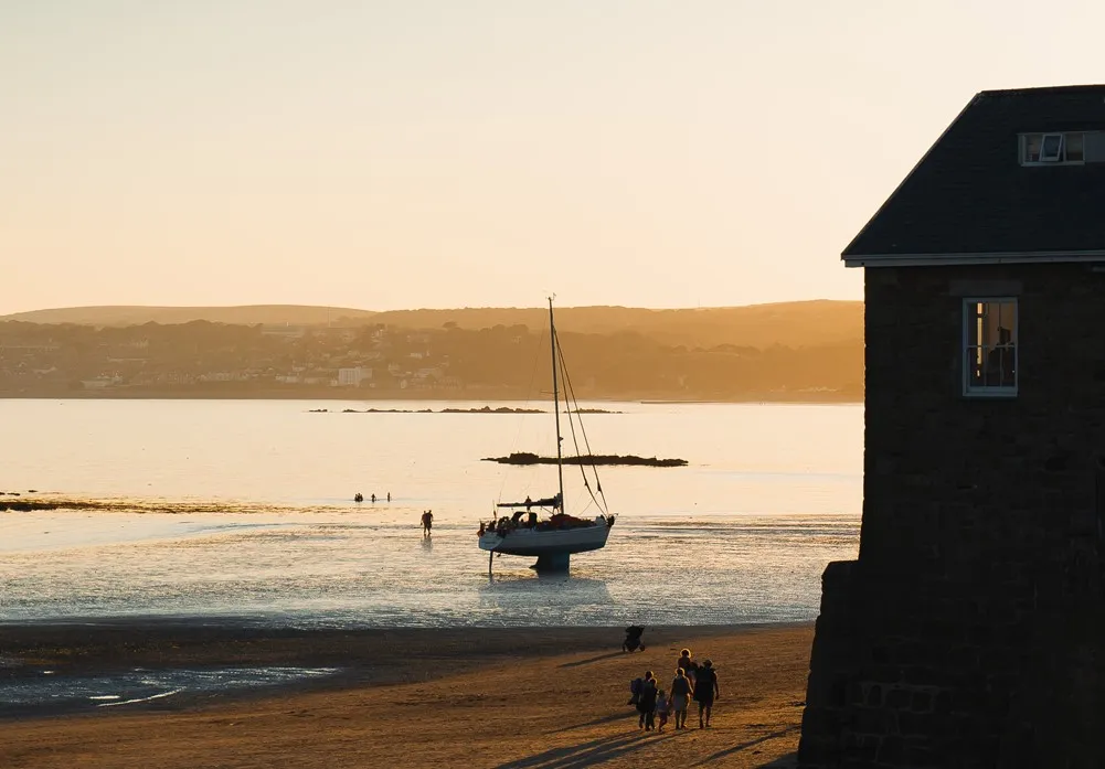 A group of people on a beach with a sailboat on the sand.