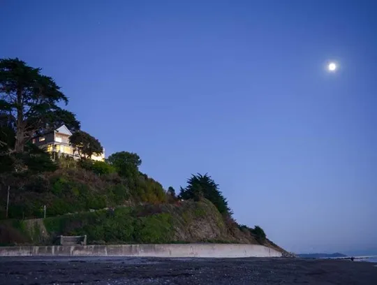 A house on a cliff amongst trees, overlooking the sea.