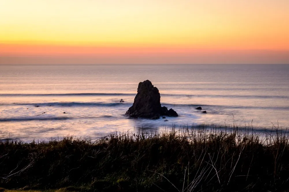 A large rock poking out from the sea at sunset.