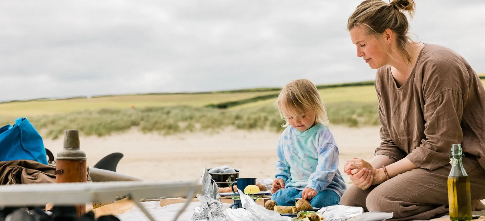 A woman and a child sitting on the beach with food.