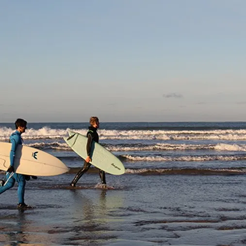 Two people walking on the beach with surfboards.