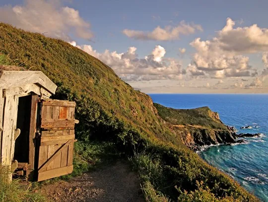 A wooden door on a hill with the sea in the background.