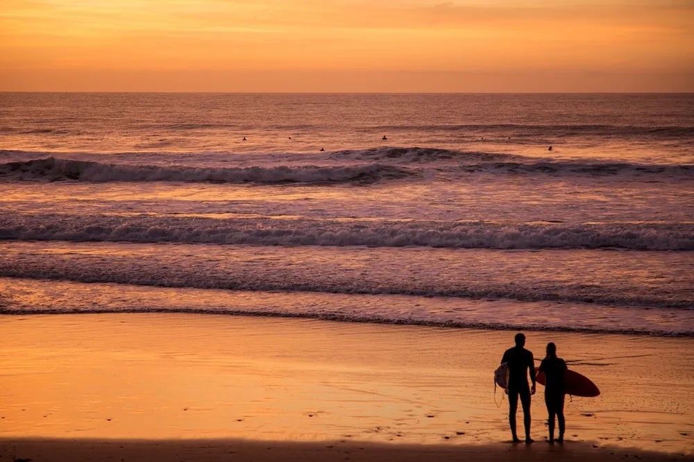 Two people holding surfboards on a beach. 