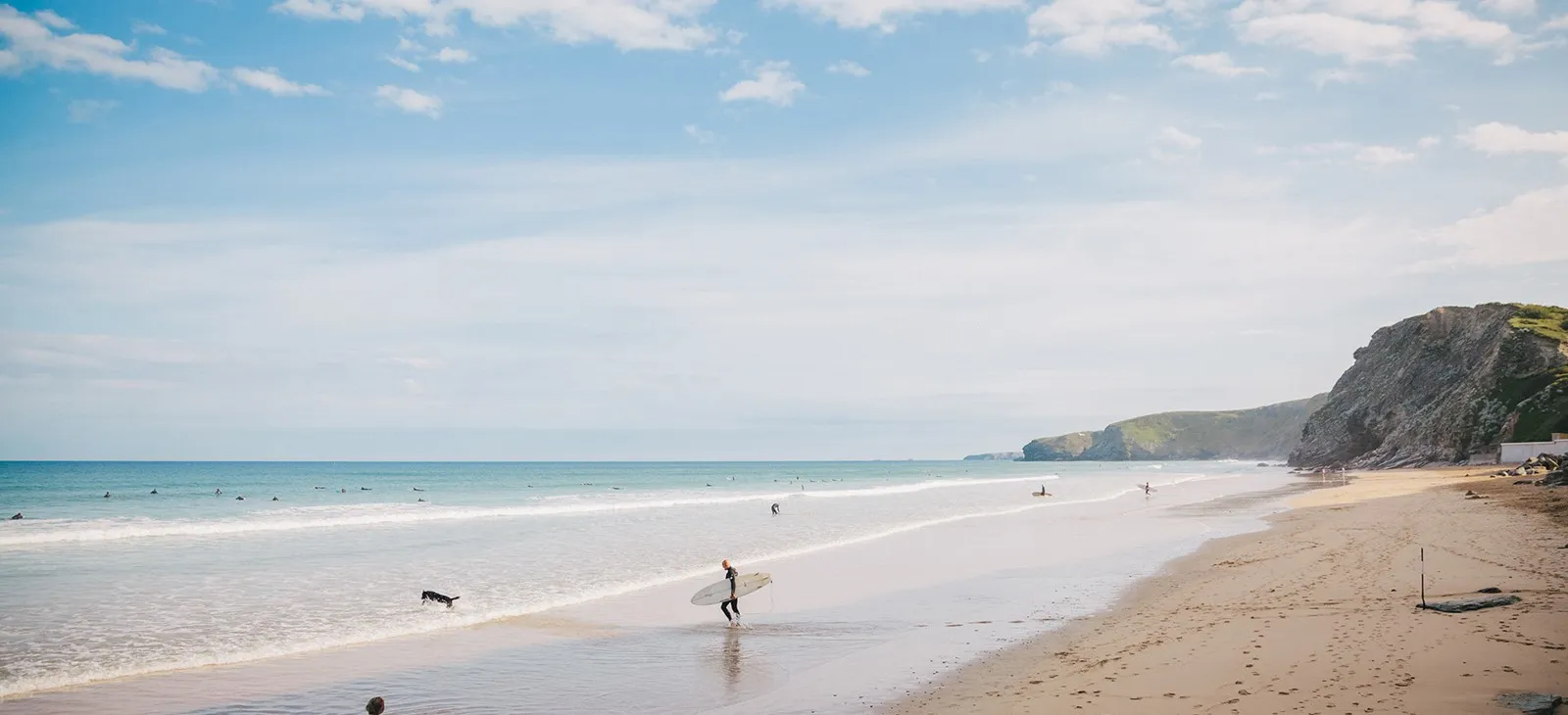 A surfer carrying a surfboard on a beach.