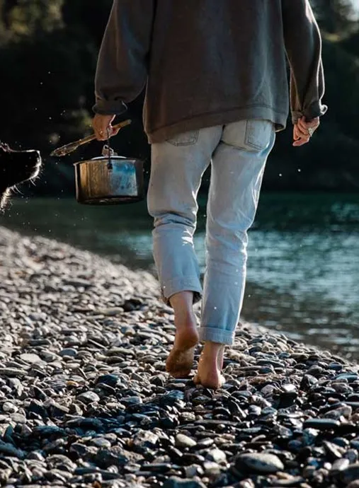 A woman walking on a rocky beach with a pot and a dog.