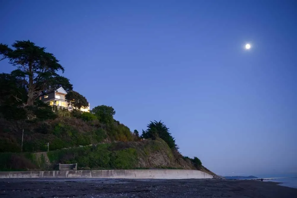 A house on a hill with trees and a moon in the sky.