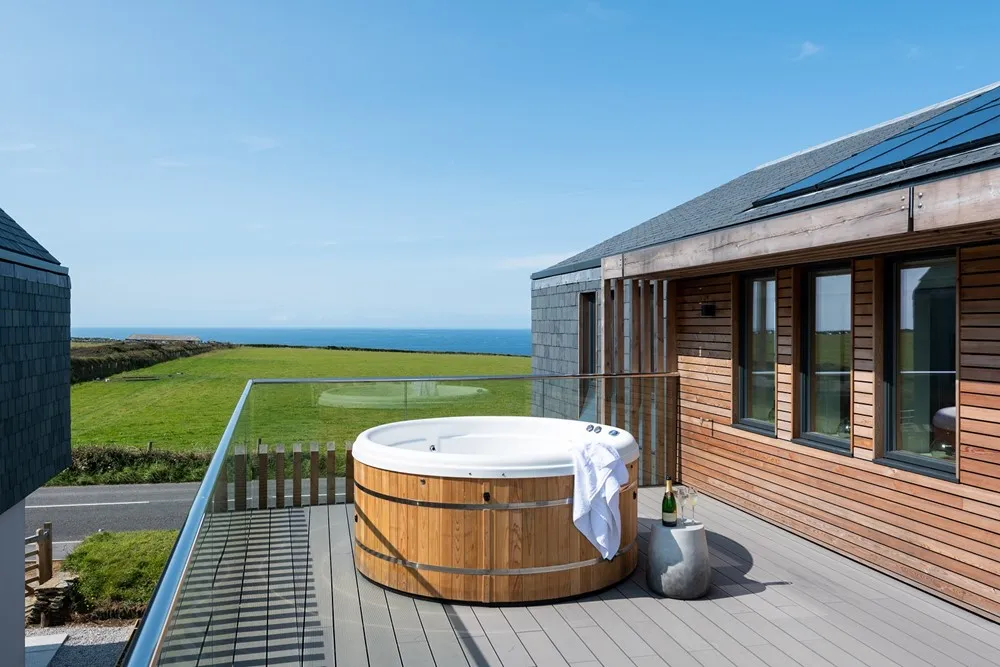 A hot tub on a deck with a glass railing and a green field.