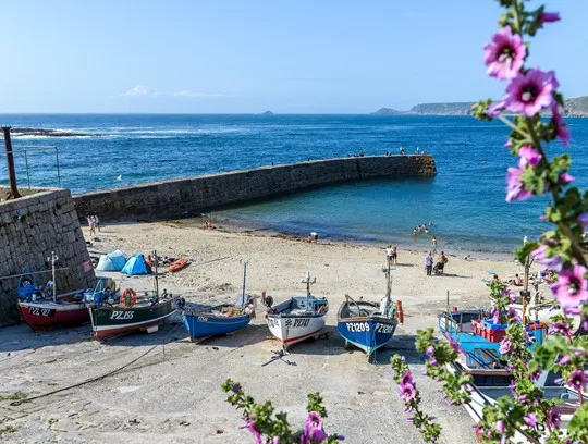 Boats on a beach with a stone wall and flowers.