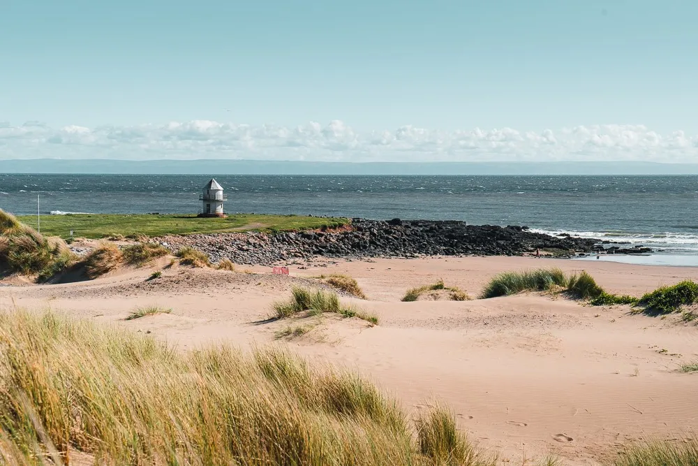 A beach with sand and grass and a small building. 