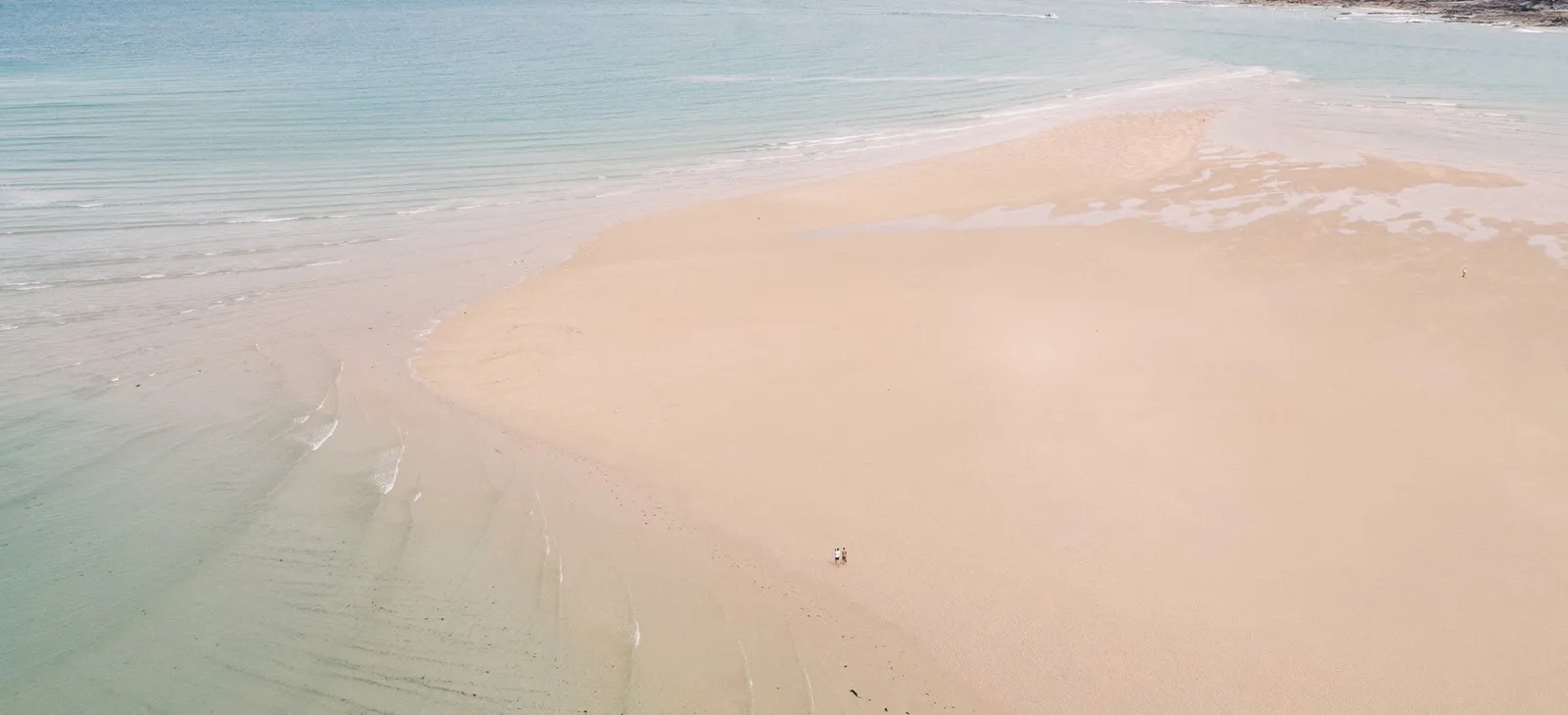 A couple of people walking on a beach.