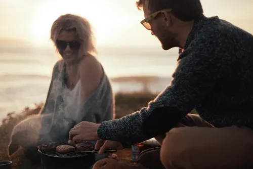 A man and woman cooking food on a grill. 