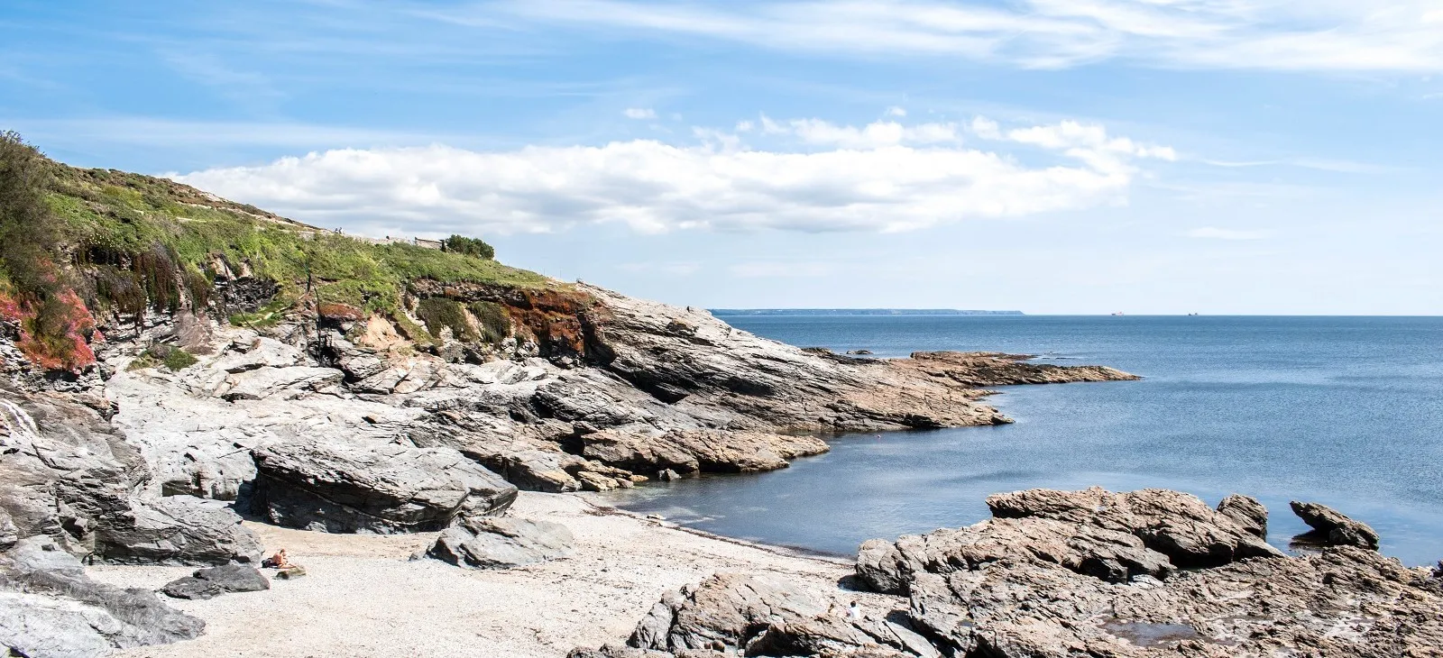 A rocky small beach overlooked by a hill.