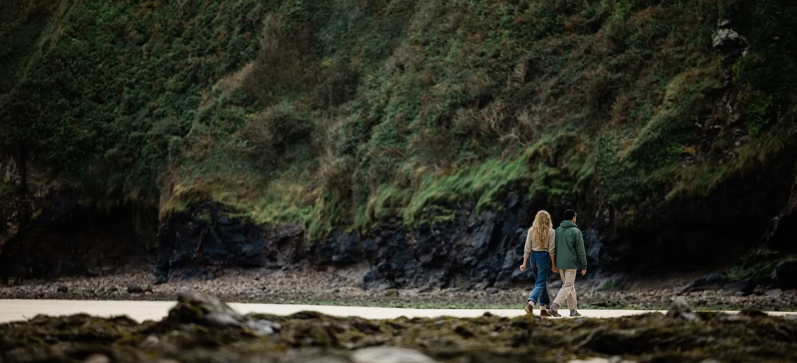 A couple walking across a rocky beach.