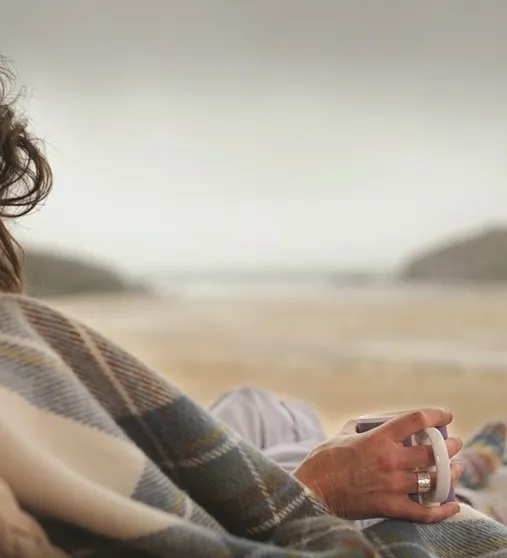 A person holding a cup on the beach.