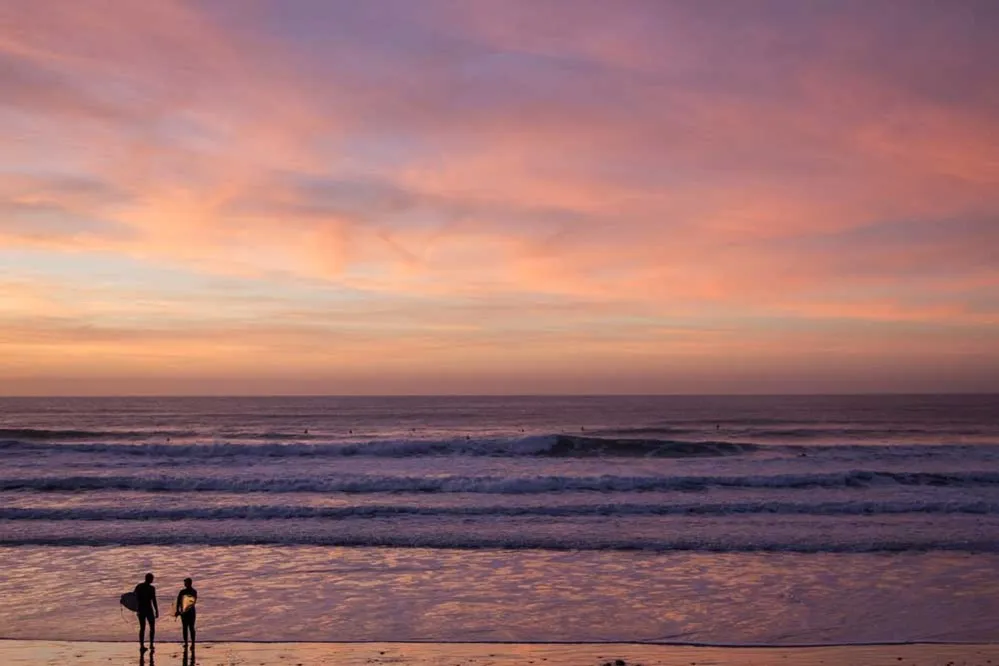 People standing on a beach with a surfboards.