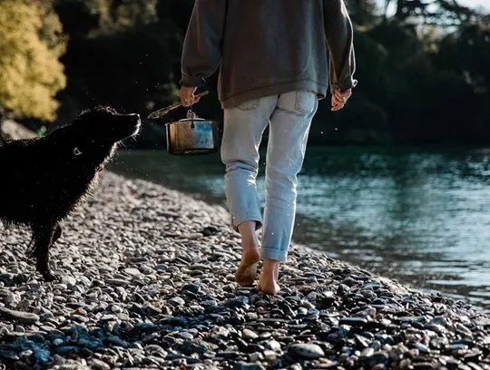 Woman and dog carrying pots on the beach in Cornwall.