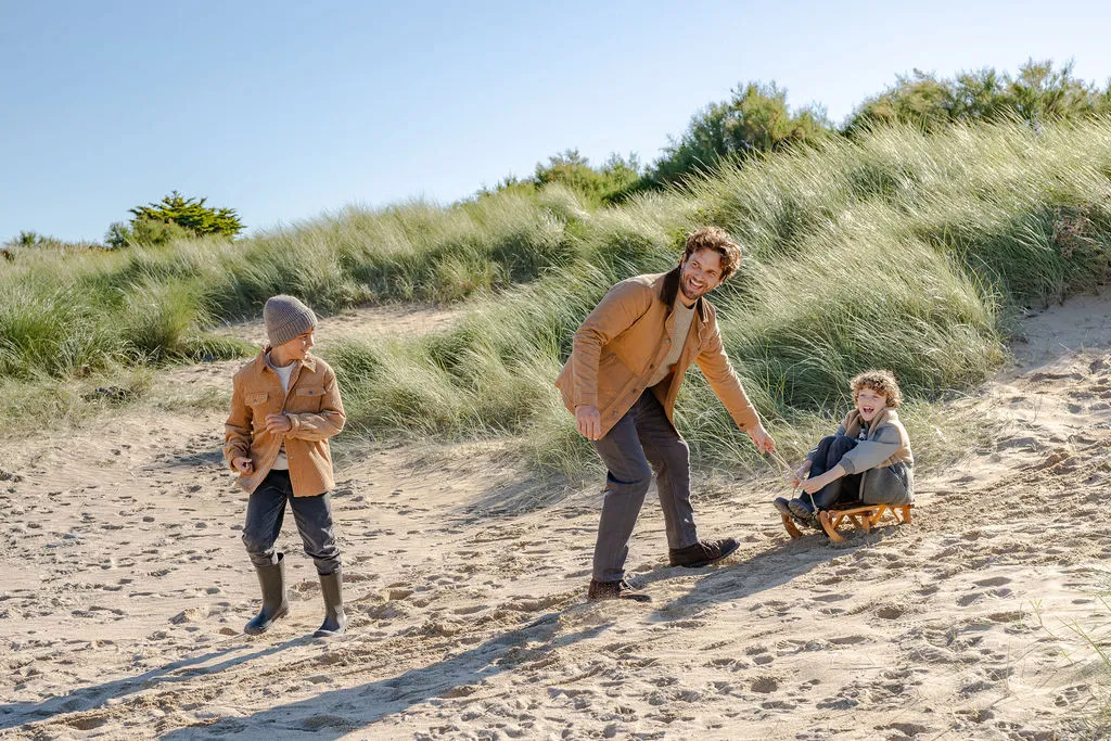 A dad and two boys playing with a toboggan on a beach